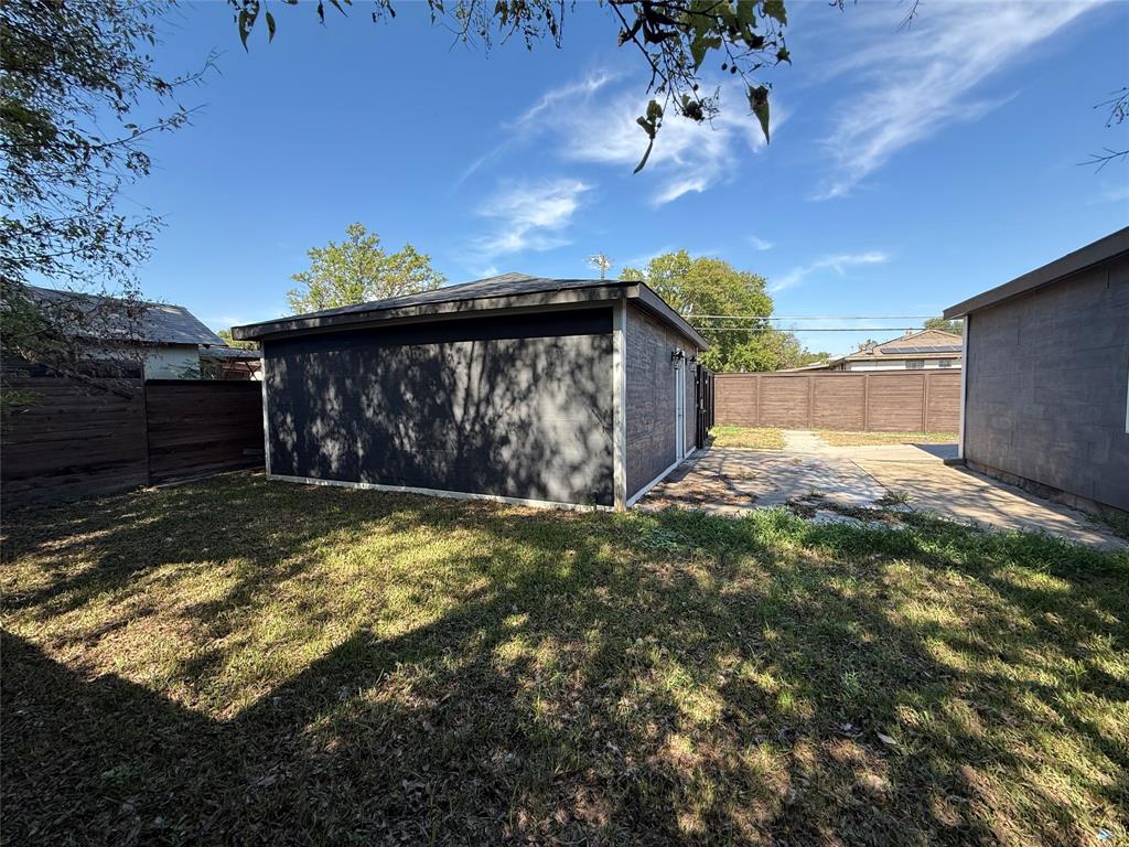 Detached structure with dark exterior cladding, paved patio area, and enclosed wooden perimeter fencing