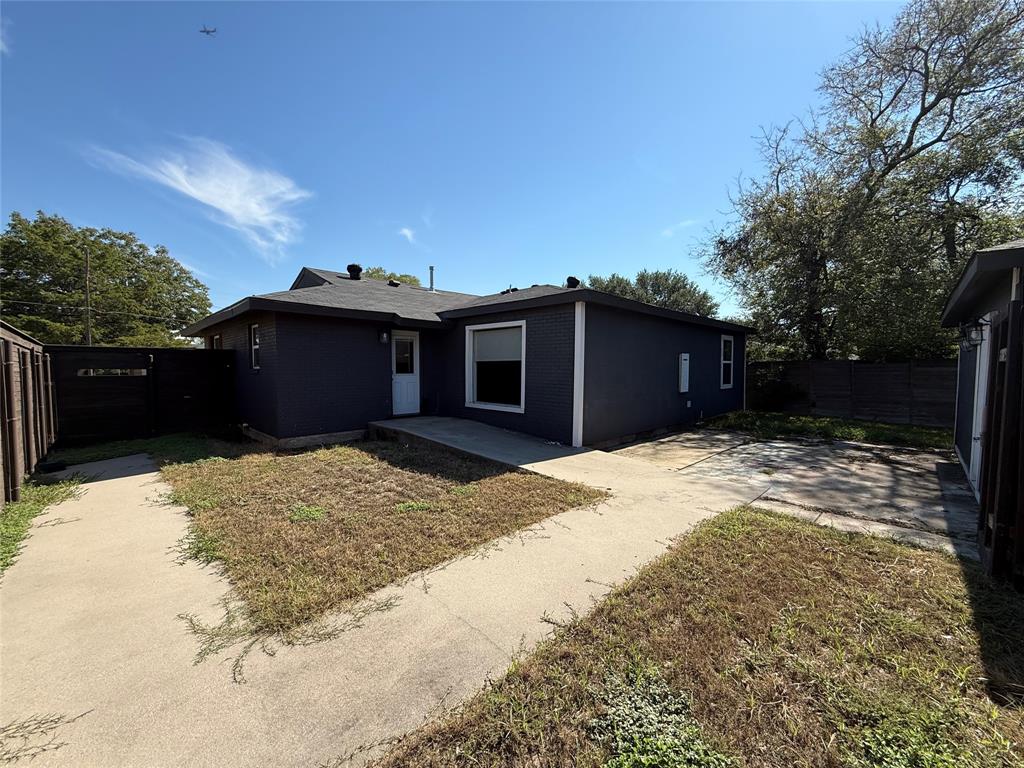 Dark-painted brick exterior featuring a multi-pitched roofline, concrete rear patio, and fenced outdoor space Dark-painted brick exterior featuring a multi-pitched roofline, concrete rear patio, and fenced outdoor space