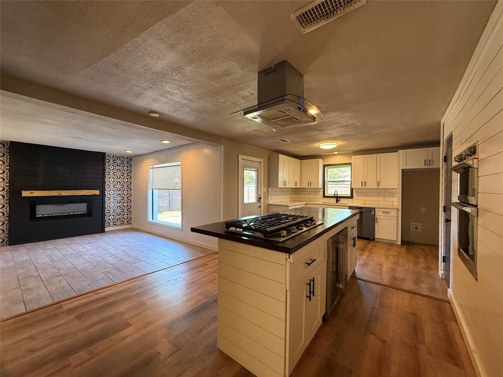 Kitchen featuring white cabinetry, center island with gas cooktop, built-in double wall oven, and wood-finish flooring