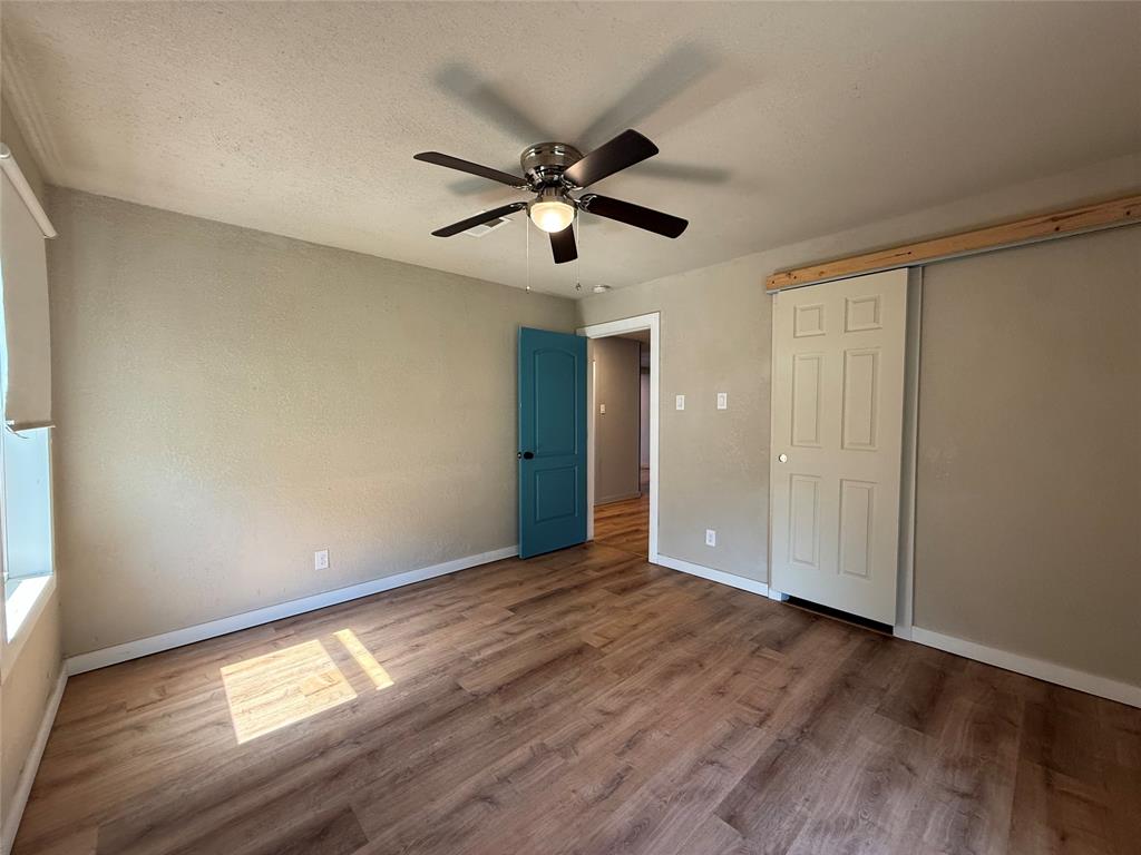 Room featuring wood-finish flooring, a ceiling fan with integrated light fixture, a blue paneled interior door, and a sliding closet door with a decorative wood header
