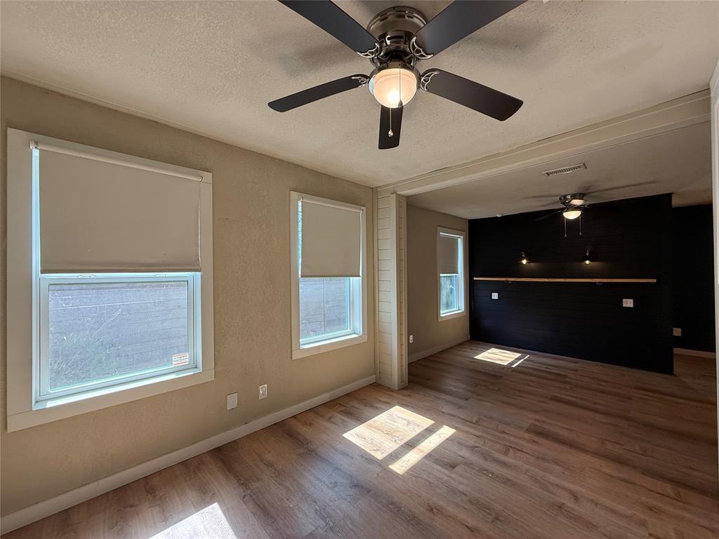 Wood-finish flooring, dark-toned accent wall, ceiling fans with integrated lighting, and neutral wall tones