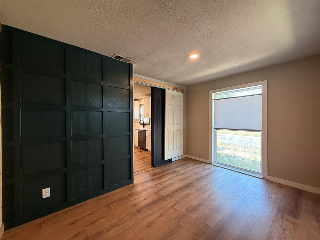 Interior space featuring grid-patterned dark accent wall, wood-finish flooring, sliding barn-style door, and large window with cellular shade