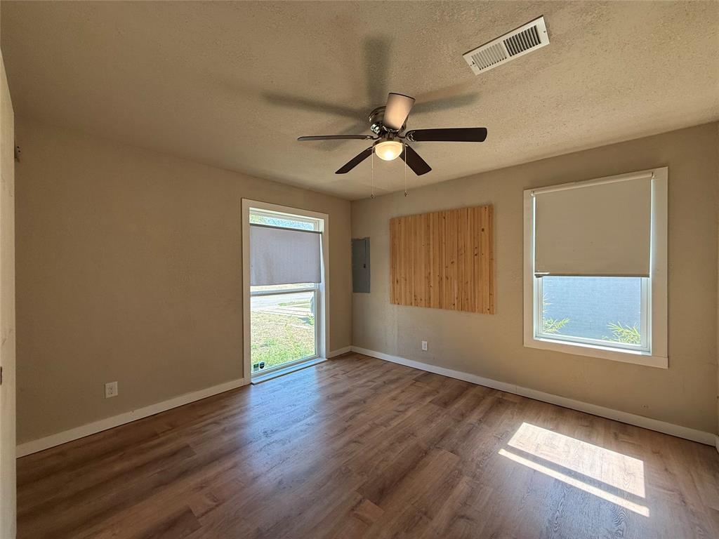 Room featuring wood-finish flooring, two windows with roller shades, and a ceiling fan with integrated lighting