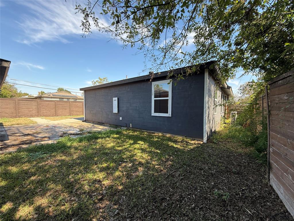 Exterior of the residence featuring painted masonry siding, a single-hung window, and a paved hardscape area enclosed by perimeter fencing
