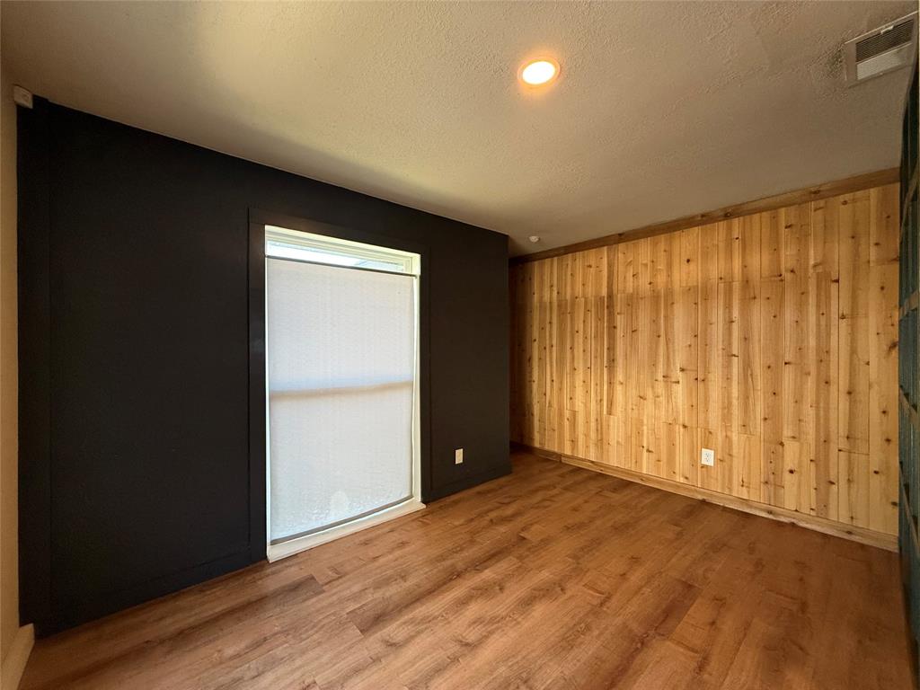 Room featuring wood-finish flooring, vertical natural wood paneling, contrasting dark-toned wall, and recessed lighting