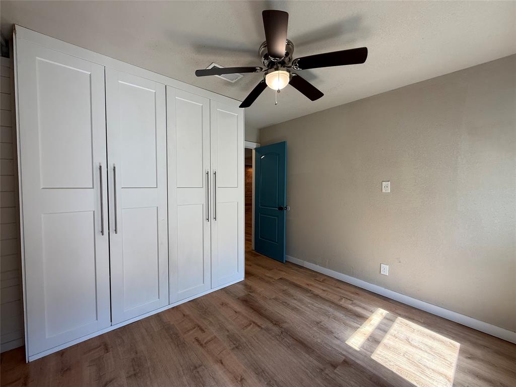 Built-in floor-to-ceiling cabinetry with shaker-style doors, wood-finish flooring, ceiling fan with integrated light fixture, and paneled door