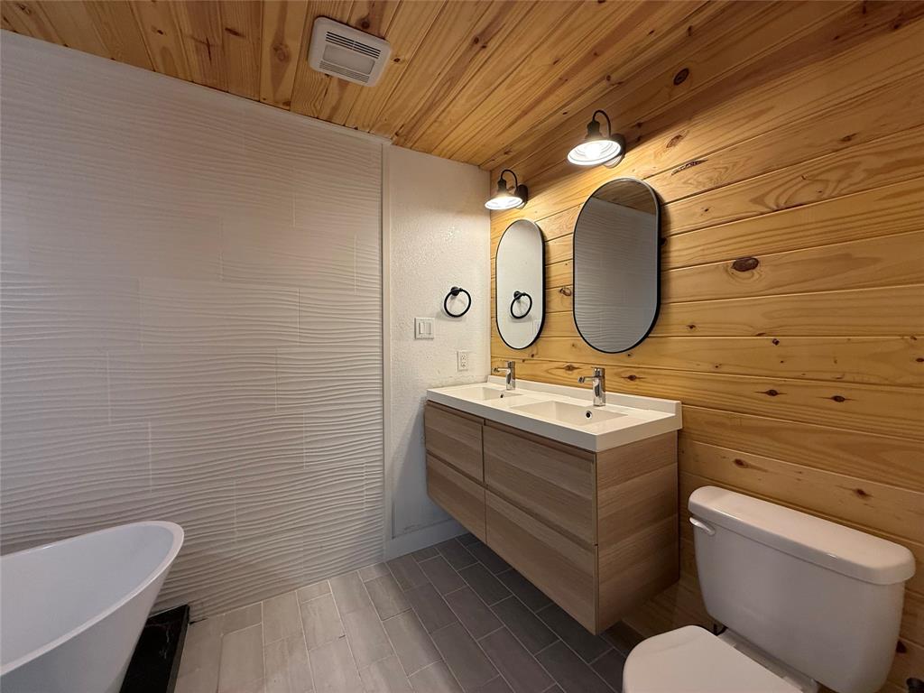 Floating dual-sink vanity with a solid-surface countertop, wood-paneled walls and ceiling, textured wall tile, and a freestanding soaking tub