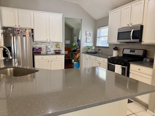 Kitchen featuring white shaker-style cabinetry, solid-surface countertops, a stainless steel refrigerator, a built-in microwave, and a tiled backsplash