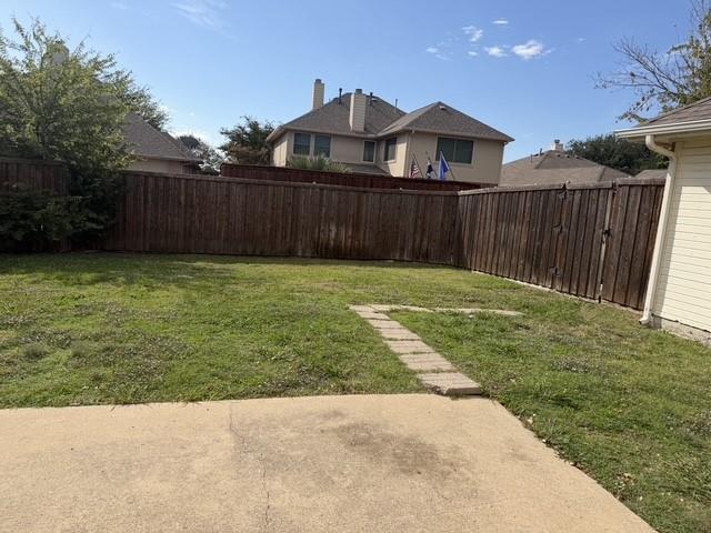 Rear exterior area featuring a concrete patio, stone paver pathway, grass yard, and full-height wood privacy fencing