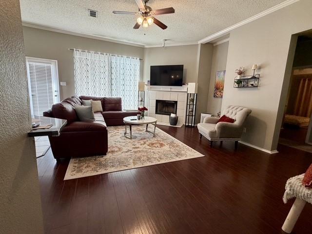 Living area featuring wood-finish flooring, a tiled fireplace with a mantle, and a ceiling fan with integrated lighting