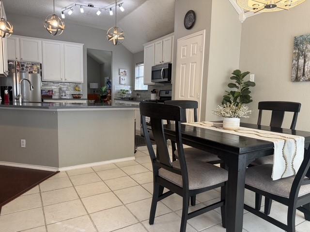 Kitchen featuring white cabinetry, solid-surface countertops, tile flooring, spherical pendant lighting, and vaulted ceilings