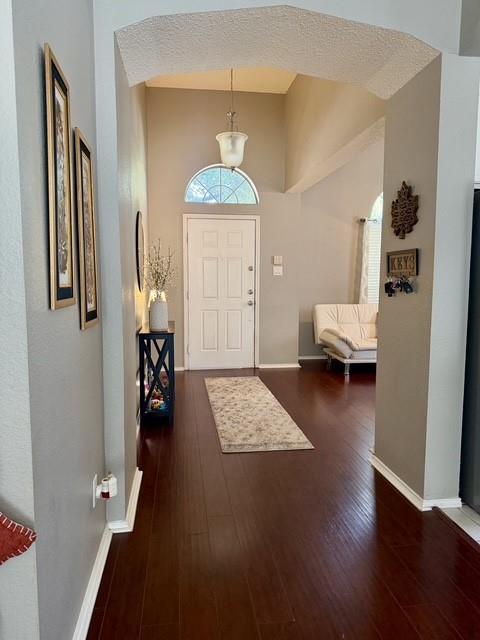 Entryway featuring high ceilings, arched architectural detailing, wood-finish flooring, a pendant light fixture, and a white front door with a half-moon transom window