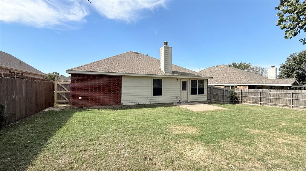 Backyard featuring a grass lawn, paved patio, red brick and horizontal siding exterior, masonry chimney, and wood privacy fencing