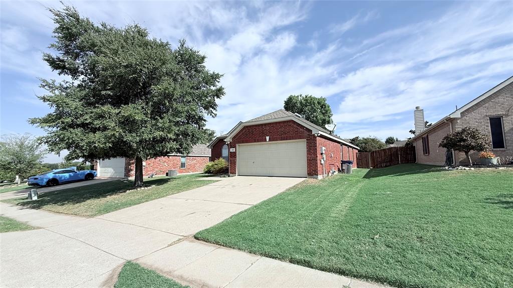 Red brick exterior featuring an attached two-car garage, concrete driveway, and front lawn