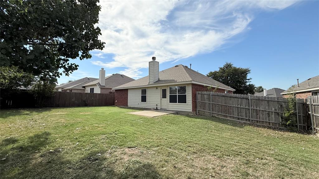 Rear exterior featuring a brick and siding facade, concrete patio, masonry chimney, and wood perimeter fencing