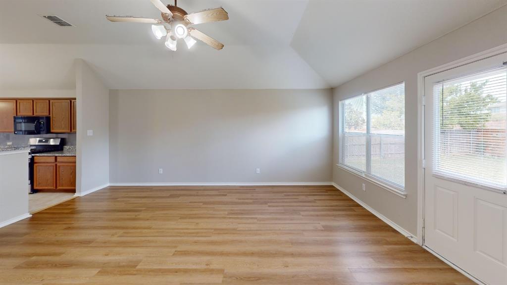 Vaulted ceiling featuring a central lighted ceiling fan, wood-finish flooring, dual windows, and an exterior door with integrated blinds