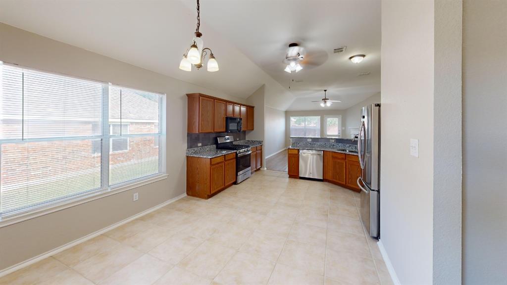 Kitchen featuring wood cabinetry, stone-finish countertops, stainless steel appliances, tile flooring, and vaulted ceilings