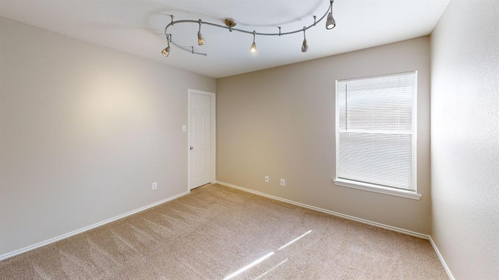 Room featuring neutral wall tones, carpeted flooring, a multi-head curved track lighting fixture, and a window with horizontal blinds