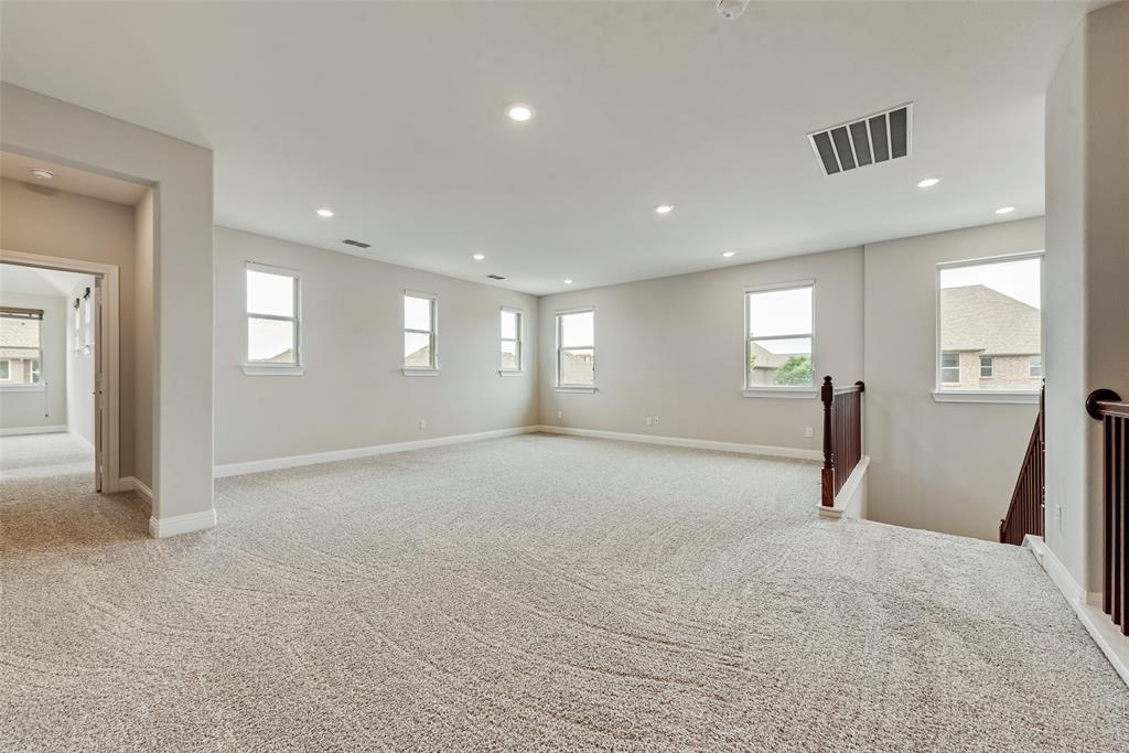 Expansive interior room featuring neutral wall tones, recessed lighting, wall-to-wall carpeting, multiple windows, and a wood-finish staircase railing