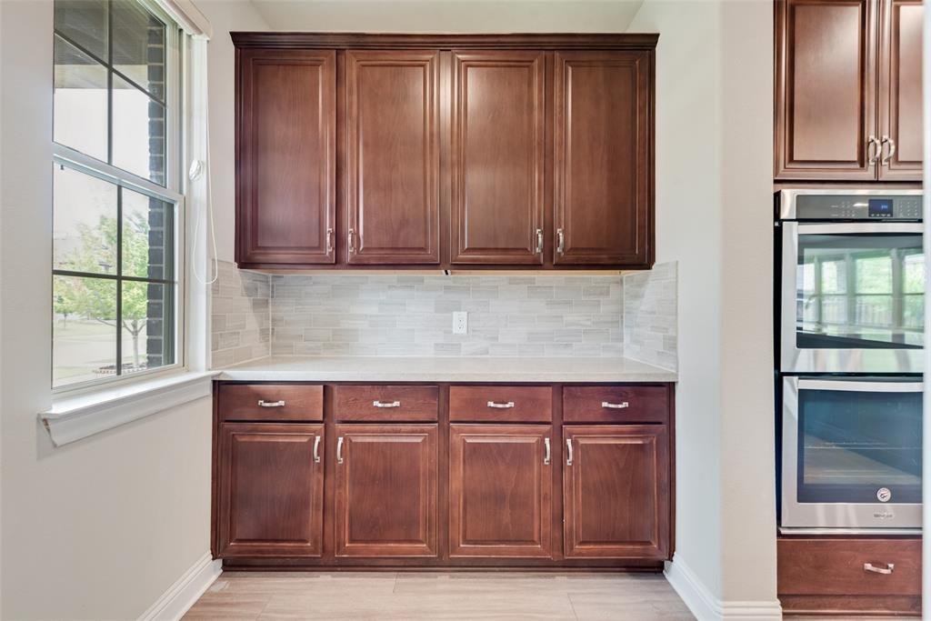 Custom cabinetry with dark wood finish, light-toned countertop, stacked tile backsplash, and built-in stainless steel double wall ovens