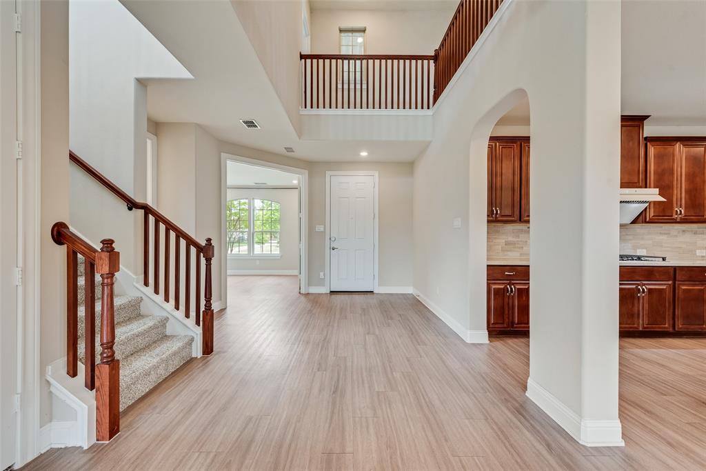 Two-story foyer featuring wood-finish flooring, a wood-railed staircase, arched architectural detailing, and custom stained-wood cabinetry