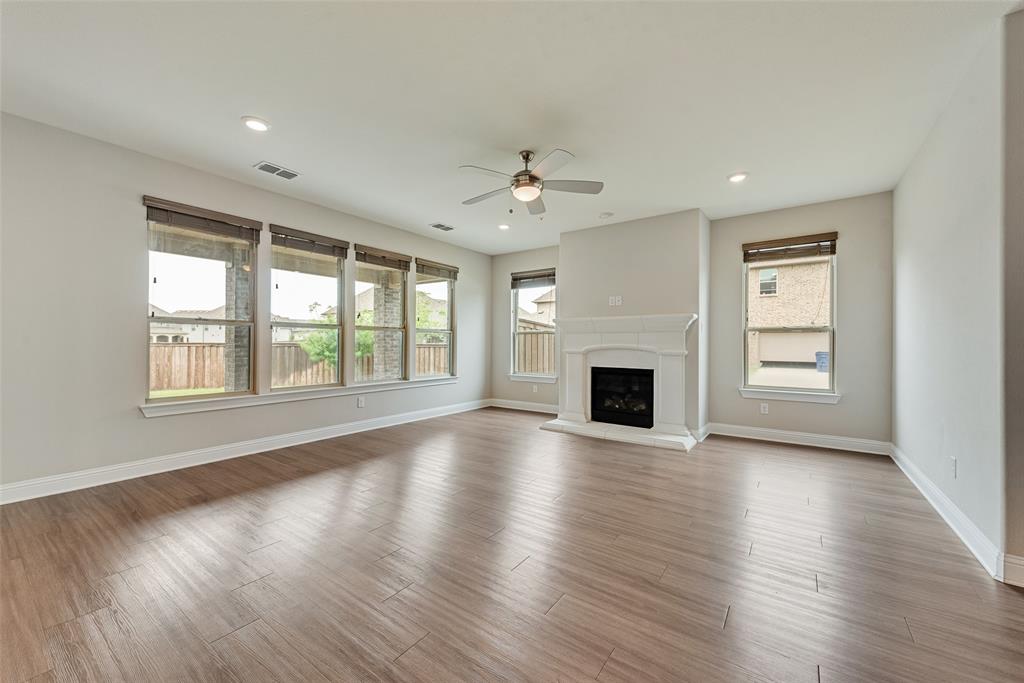 Open interior featuring wood-finish flooring, a white hearth fireplace, recessed lighting, a ceiling fan, and large windows with horizontal blinds
