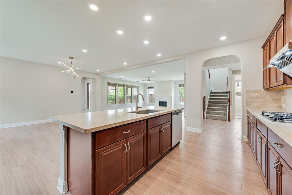 Kitchen featuring wood-finish cabinetry, a central island with an integrated stainless steel sink, recessed lighting, and tile flooring