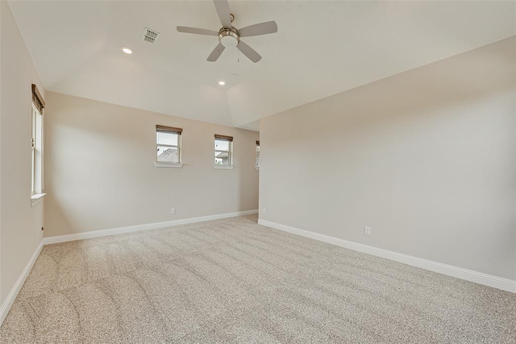 Vaulted ceilings, neutral wall color, plush wall-to-wall carpeting, multiple windows with neutral roller shades, and a ceiling-mounted fan with integrated lighting