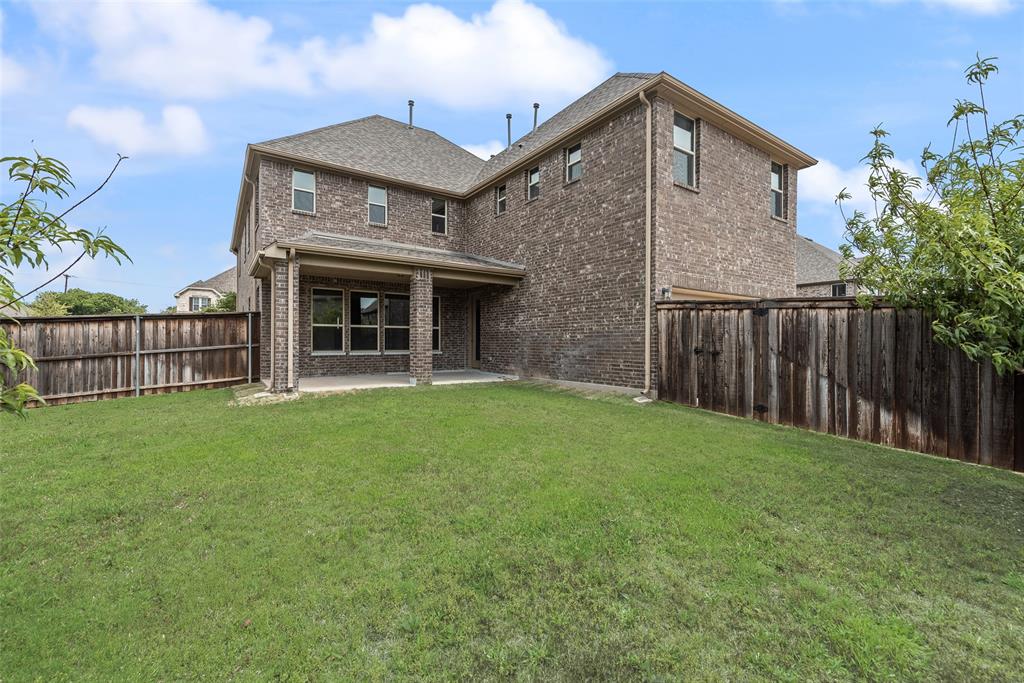 Two-story brick exterior featuring a covered patio, shingle roof, and full wood privacy fencing