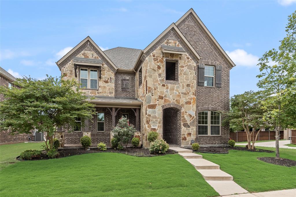 Two-story traditional exterior featuring a blend of multi-toned stone and brick masonry, covered front porch, decorative wood-finish shutters, and gabled roofline