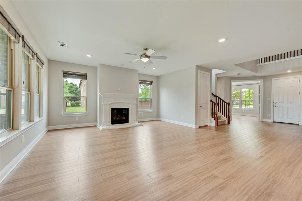 Open-concept interior featuring wood-finish flooring, a white mantel fireplace, recessed lighting, a ceiling fan, and staircase with wooden handrails