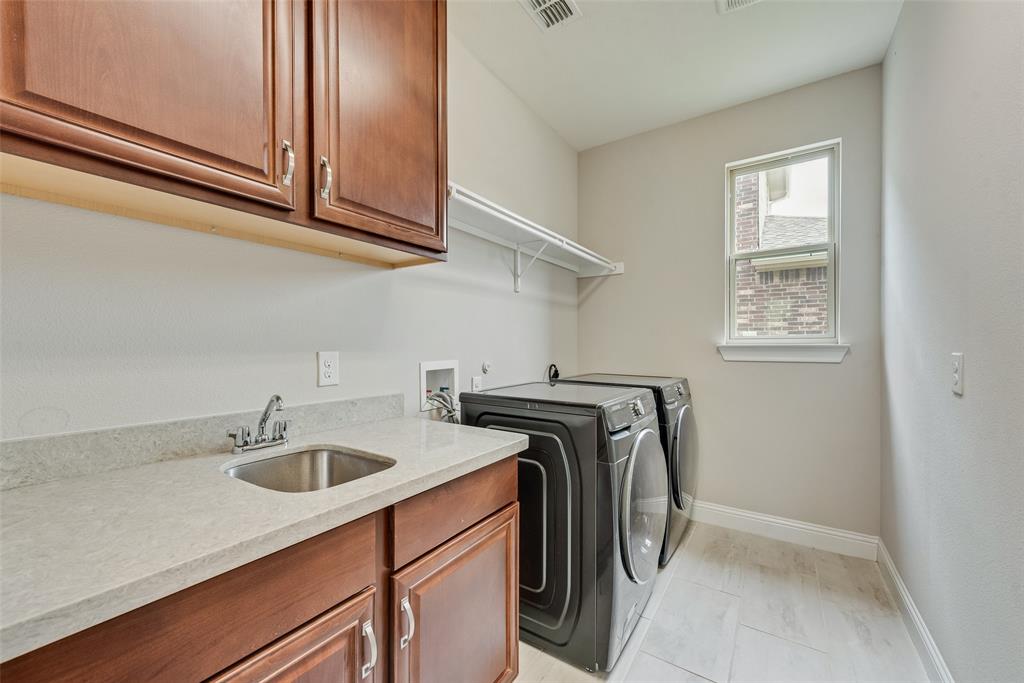 Laundry area featuring wood-finish cabinetry, solid-surface countertop, stainless steel drop-in sink with chrome faucet, and white tile flooring