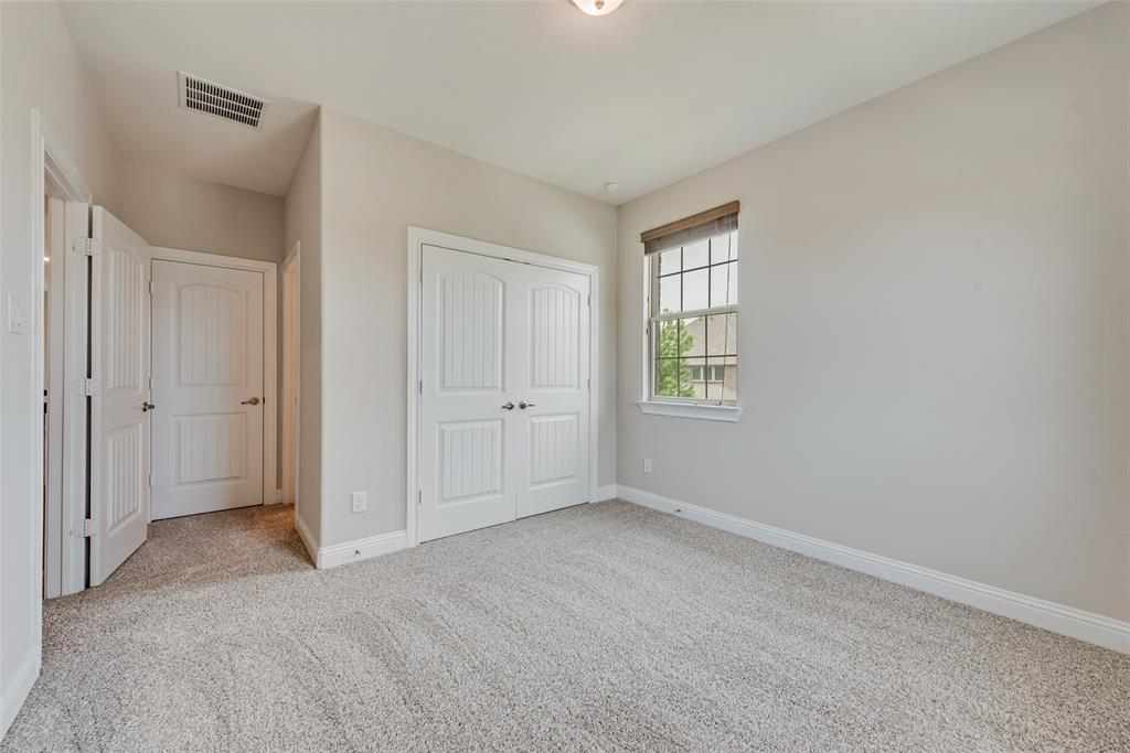 Neutral-toned interior room featuring wall-to-wall carpeting, dual-panel closet doors, a single-hung window with a wooden valance, and a flush-mount ceiling light fixture