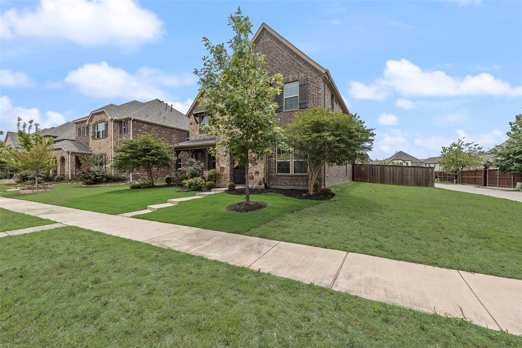 Multi-story brick exterior featuring steep roof pitches, decorative shutters, a covered entryway, and a landscaped lawn
