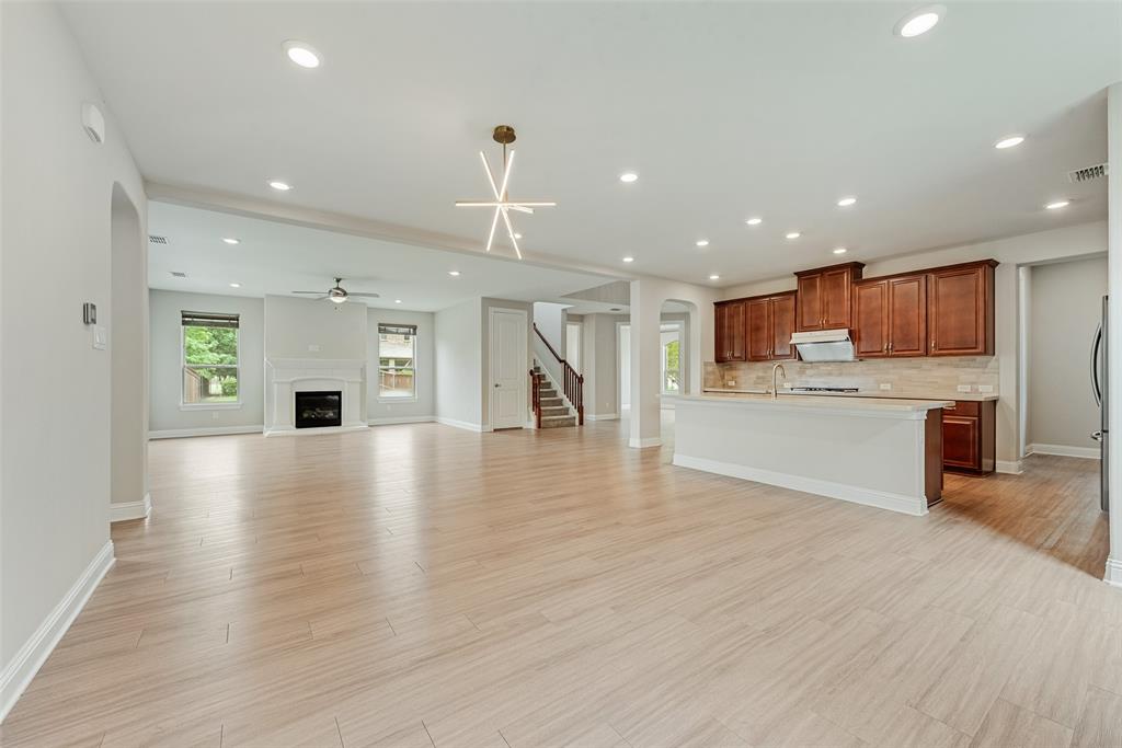 Open floor plan featuring wood-finish flooring, recessed lighting, a fireplace with a decorative mantel, a central island kitchen with wood cabinetry, and a geometric chandelier