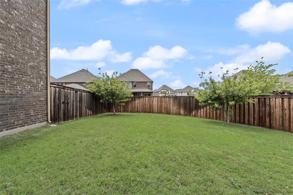 Private backyard featuring a brick exterior wall, manicured grass lawn, wood privacy fencing, and two mature trees