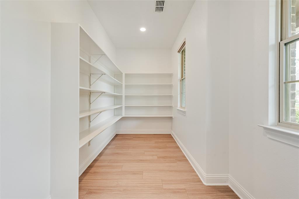 Storage space featuring wood-finish flooring, white walls, and multiple tiers of wall-mounted shelving