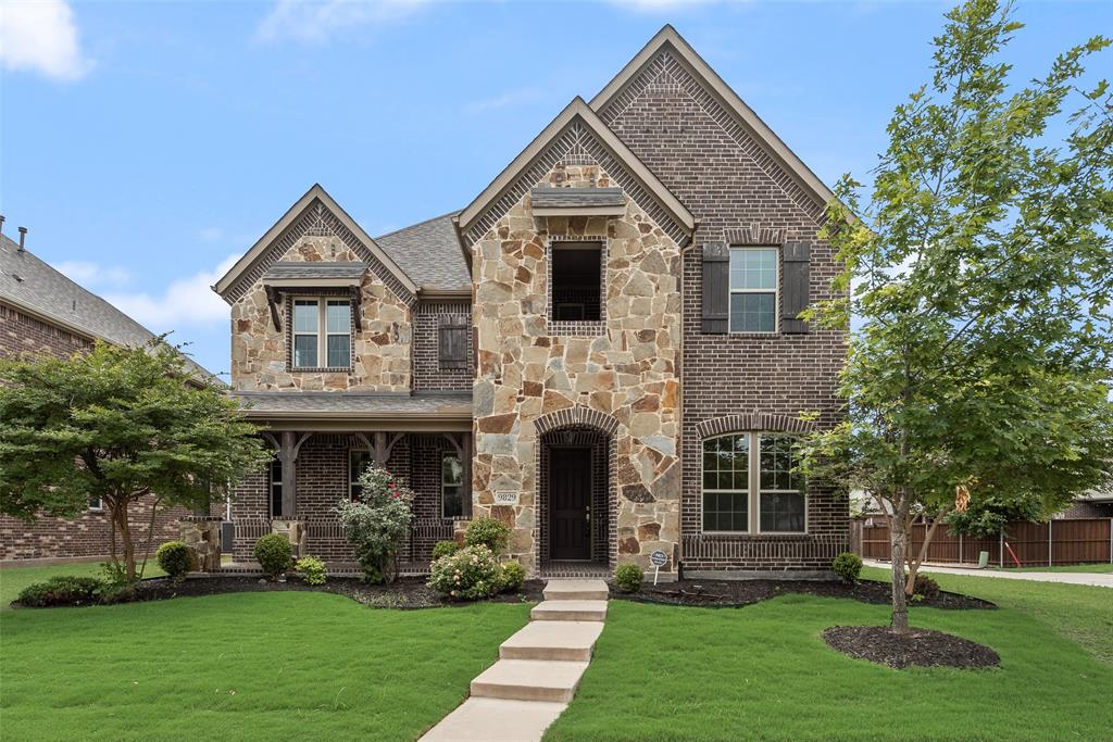 Two-story exterior featuring multi-gabled rooflines, a combination of dark brick and stone cladding, custom wood-finish shutters, and a covered front porch with timber beam detailing