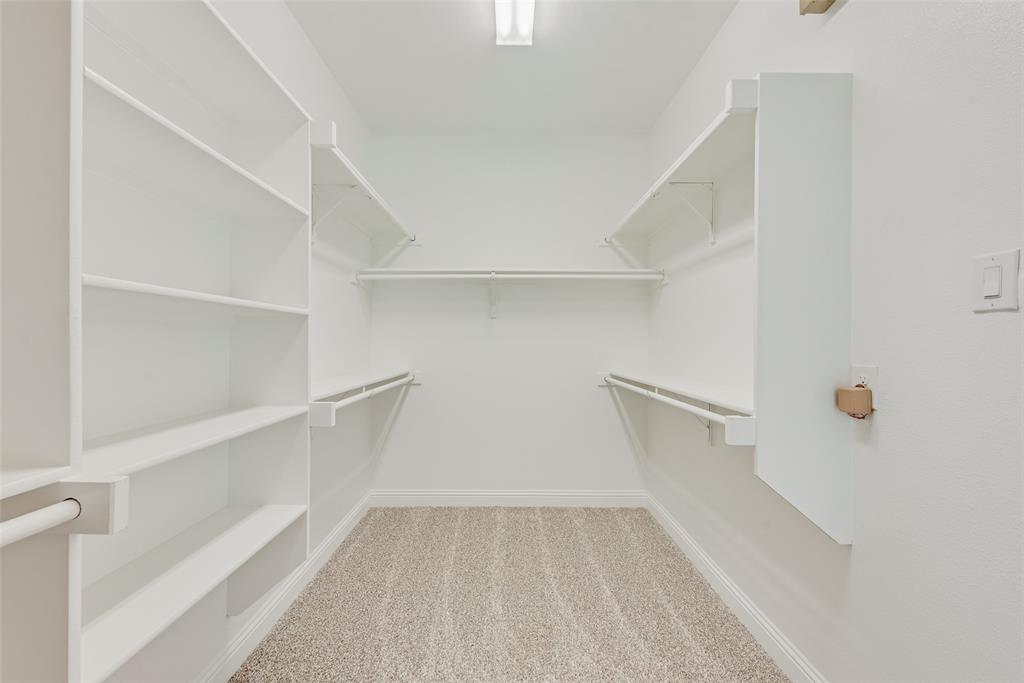Walk-in closet featuring white built-in shelving, integrated hanging rods, and neutral carpeting