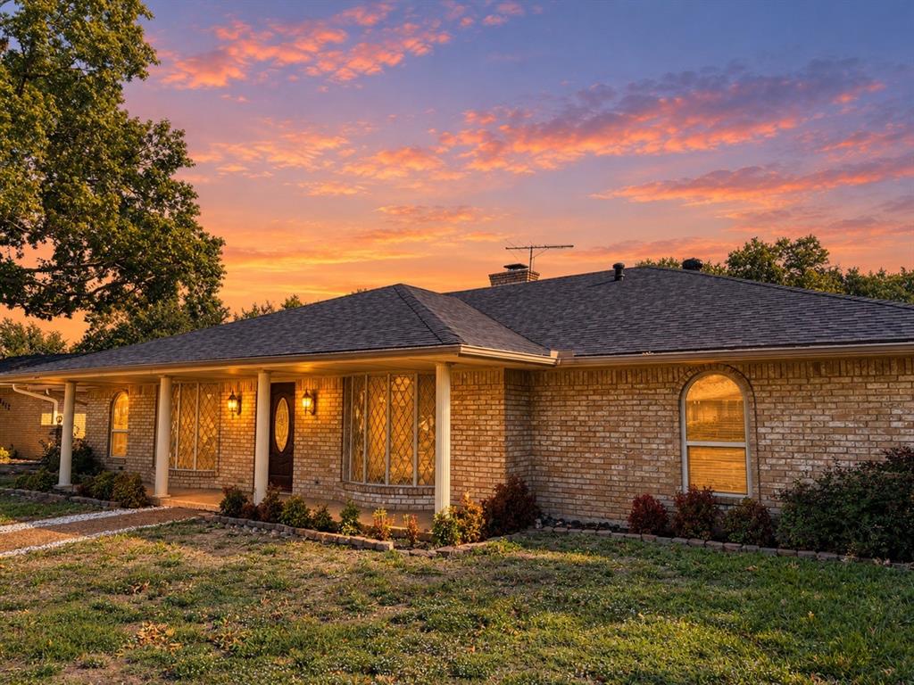 Single-story brick exterior featuring a covered front porch, arched window detailing, and a shingled hip roof