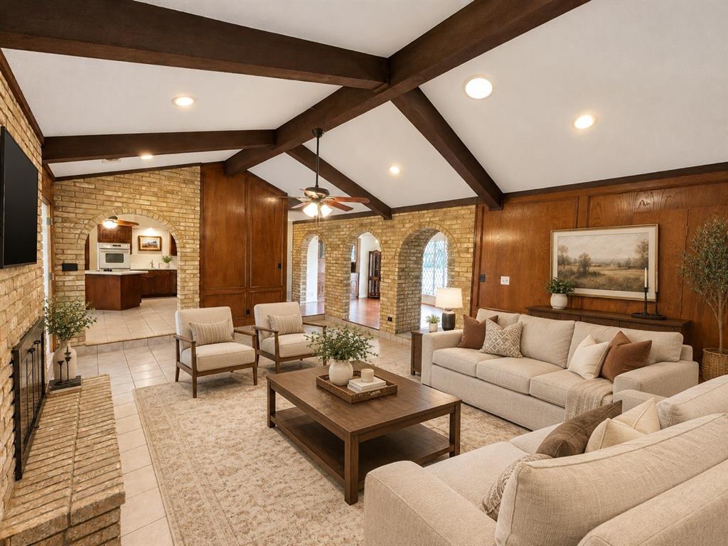 Vaulted ceiling with exposed wood beams, brick masonry fireplace, wood wall paneling, and arched brick entryways