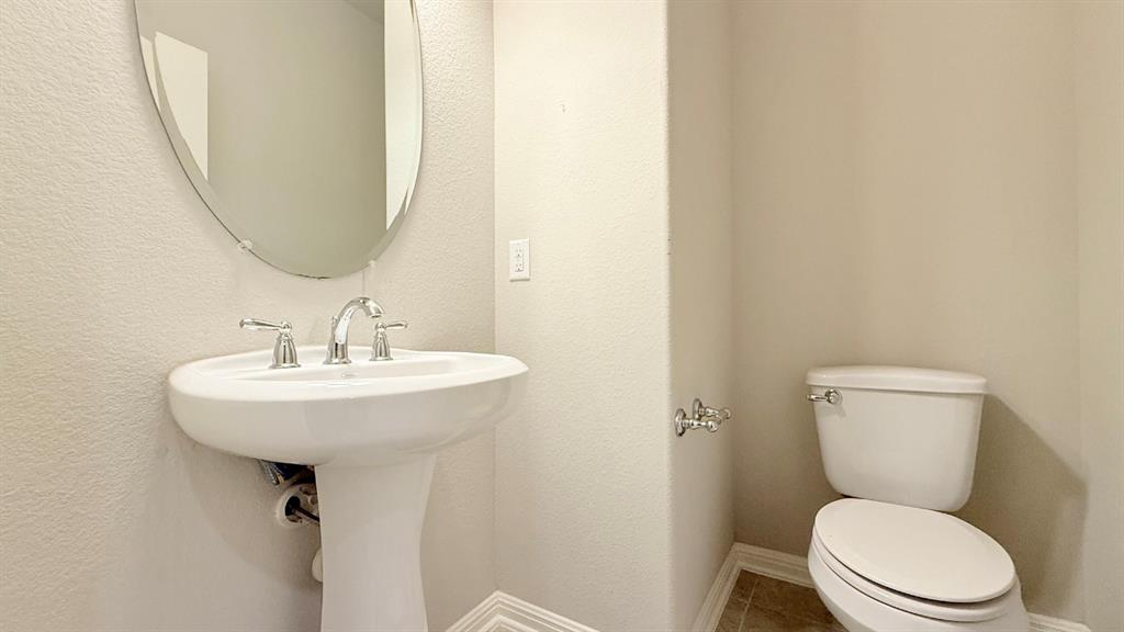 Pedestal sink with polished chrome widespread faucet, oval wall-mounted mirror, and tile flooring