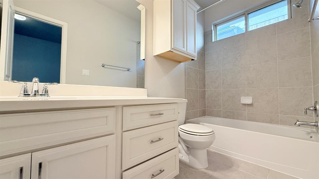 Bathroom featuring a white vanity with drawers and cabinets, a large wall-mounted mirror, a tub-shower combination with tile surround, and an upper wall cabinet