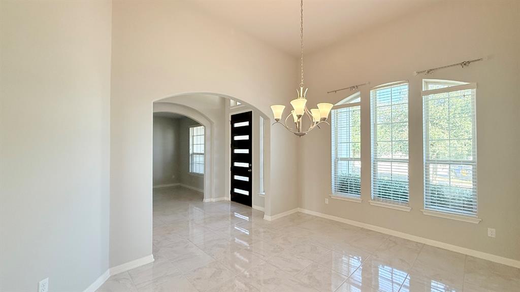 High ceilings featuring an arched entryway, polished stone-finish tile flooring, a multi-arm chandelier, and tall windows with horizontal blinds