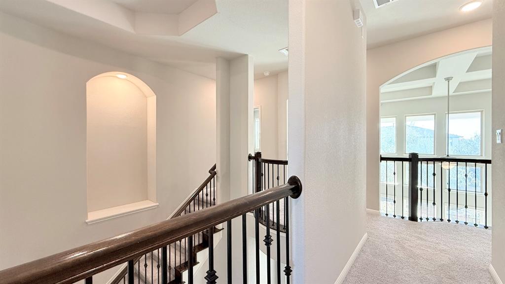 Stairway featuring an arched wall niche, wrought-iron balusters, and a wooden handrail, leading to a landing with a coffered ceiling and arched entryway