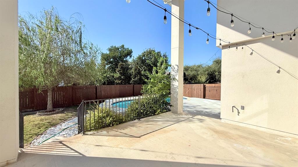 Covered patio featuring concrete flooring, swimming pool with metal safety fencing, and wood-panel perimeter privacy fencing