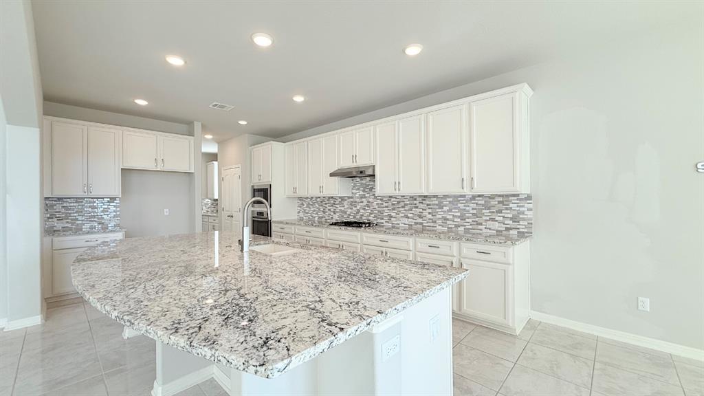 Kitchen featuring a large center island with stone countertop, white cabinetry, integrated stainless steel appliances, multi-tonal backsplash, and recessed lighting