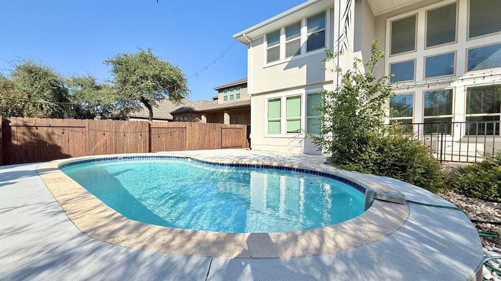 Backyard pool with concrete decking, perimeter wood fencing, and multi-story exterior with large windows