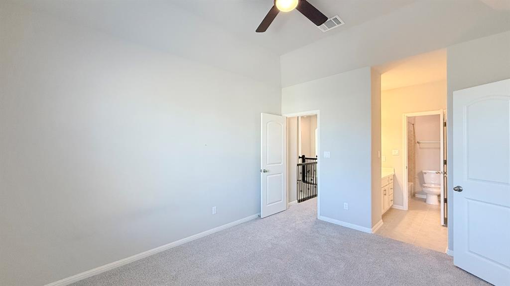 Spacious room with high ceilings, neutral wall color, plush carpeted flooring, and a mounted ceiling fan, featuring an attached bathroom with white cabinetry