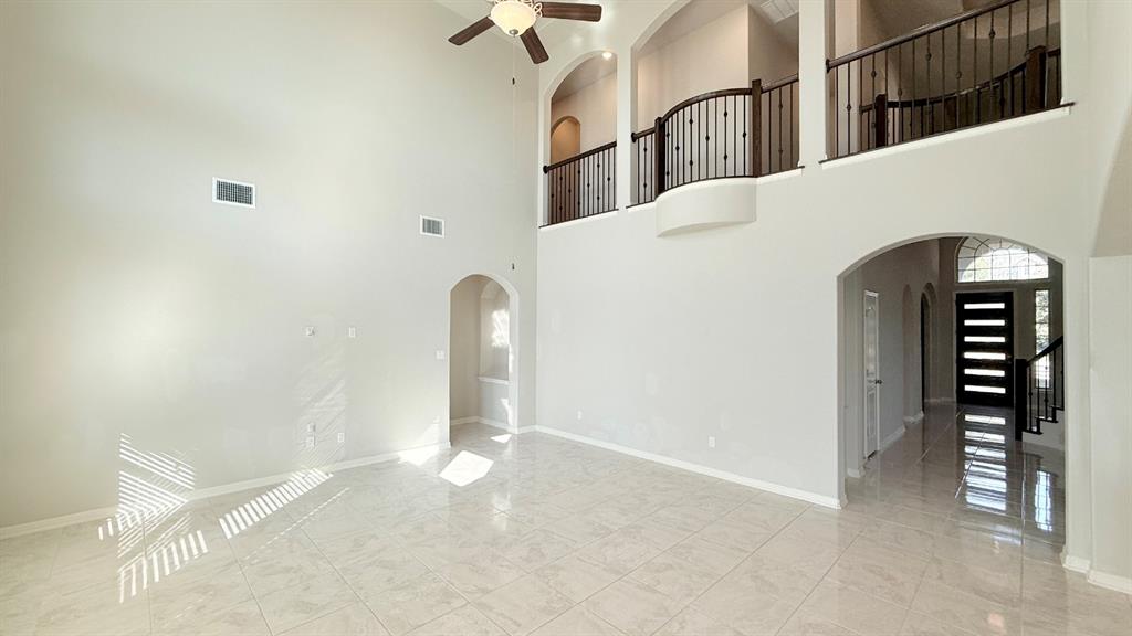 Double-height ceiling, polished tile flooring, wrought iron staircase railing, arched architectural detailing, and integrated ceiling fan